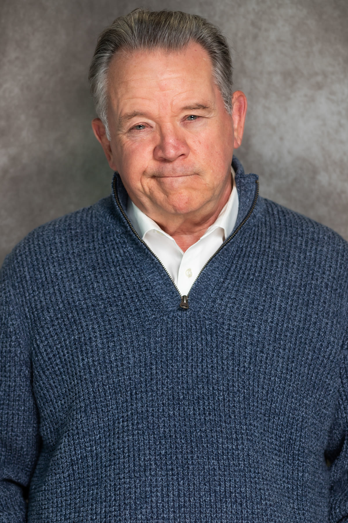 Gary Mason in a blue sweater and white shirt against a gray background